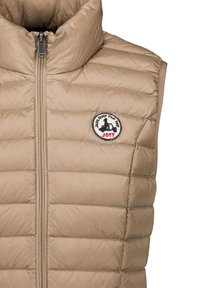 Beige doorgestikte, mouwloze donsbodywarmer met hoge kraag, ritssluiting aan de voorkant en een ronde patch met een scooterrijder en de tekst "JOTT".