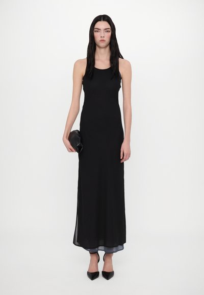 Rochie maxi neagră fără mâneci, cu un design ajustat și fante laterale, combinată cu pantofi negri cu vârf ascuțit și o geantă de mână.
