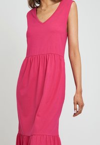 Ärmelloses pinkes Baumwollkleid mit V-Ausschnitt, gerafftem Taillenbund und ausgestelltem Saum. Die weiche Textur und die schlichte Silhouette erhöhen den Reiz des Kleides.