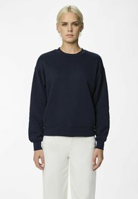 Felpa blu navy in una vestibilità ampia, con scollo a girocollo, polsini e vita a costine. Tessuto morbido, abbinata a pantaloni bianchi.