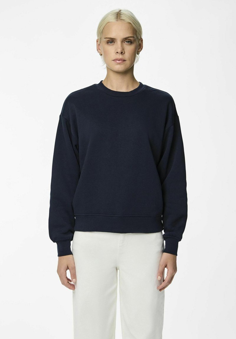 Felpa blu navy in una vestibilità ampia, con scollo a girocollo, polsini e vita a costine. Tessuto morbido, abbinata a pantaloni bianchi.