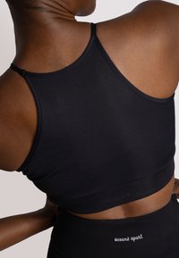 Bra sportivo nero a costine con spalline sottili, caratterizzato da una finitura testurizzata e un logo sulla parte inferiore. Progettato per comfort e supporto.