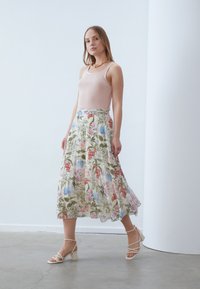 Light pink ribbed tank top paired with a flowing, floral midi skirt featuring green, blue, and red patterns. Strappy beige block-heeled sandals.