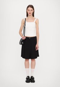 Crop top blanc avec un motif texturé, associé à une jupe plissée noire. Sac à épaule noir et chaussures noires chunky avec boucles. Chaussettes blanches.