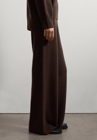 Brown knit sweater and wide-leg pants made of soft fabric. Pants drape smoothly, featuring a straight cut. Black slide sandals visible on feet.