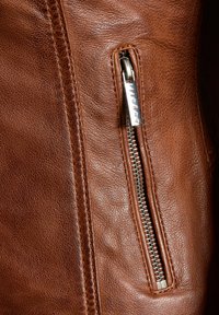 Bruine leren jack met een gestructureerd oppervlak, zichtbare stiksels en een zilveren rits aan de linkerkant voor sluiting.