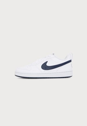 Baskets basses blanches avec le logo Nike swoosh bleu foncé et une semelle en caoutchouc, vues de profil sur un fond clair uni.