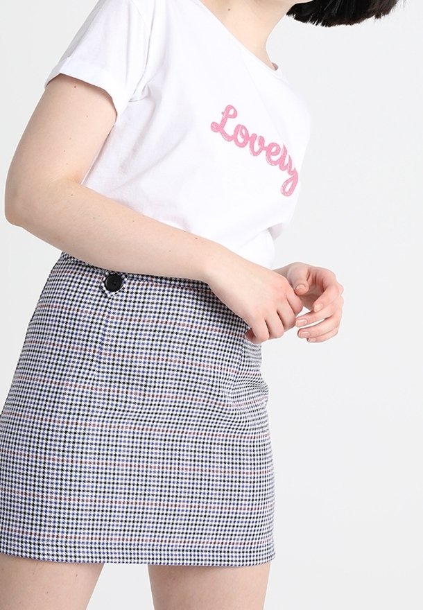 T-shirt blanc avec le texte rose "Lovely", assorti à une mini-jupe à carreaux noir et blanc avec un bouton latéral et une texture lisse.