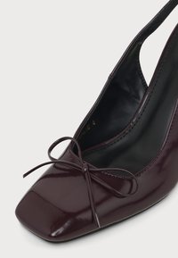 Chaussure slingback en cuir verni violet foncé avec bout carré et petit nœud sur l'empeigne avant.
