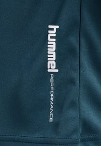 T-shirt de sport bleu foncé avec un design élégant, une texture douce et un logo imprimé blanc "hummel PERFORMANCE" sur le côté.
