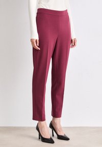 Bordeauxkleurige, slim-fit broeken gemaakt van een soepele, stretchy stof met een hoge taille, gecombineerd met zwarte puntige hakken.