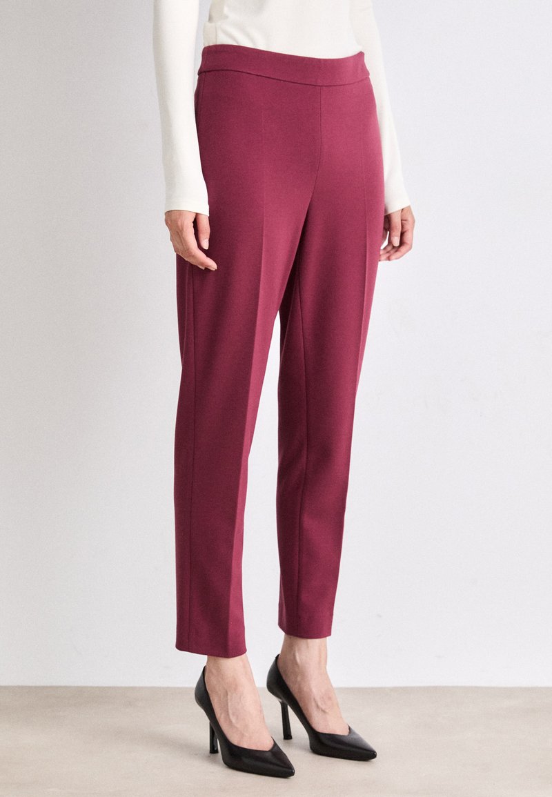 Bordeauxkleurige, slim-fit broeken gemaakt van een soepele, stretchy stof met een hoge taille, gecombineerd met zwarte puntige hakken.