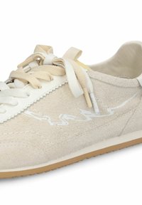 Baskets en daim beige avec des surpiqûres en zigzag blanches, des lacets couleur crème et une semelle en caoutchouc gomme, vues de côté.