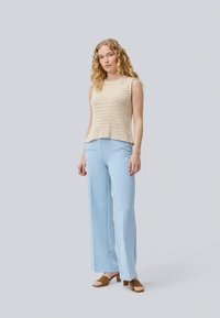 Top sem mangas em croché bege com bordas em forma de onda, combinado com calças largas em azul claro e sandálias castanhas. Design minimalista.