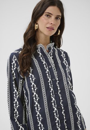 Cămașă bleumarin cu nasturi, cu broderie florală albă, având un guler ondulat și mâneci lungi. Material din bumbac, croi lejer.