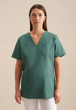 Grüne Kurzarm-Tunika mit V-Ausschnitt, versehen mit einer Brusttasche und zwei Seitentaschen. Hergestellt aus einem glatten, leichten Stoff.