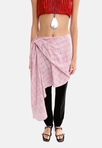 Różowa kraciasta spódnica w formie narzutki na czarne spodnie, połączona z brązowymi płaskimi sandałami, wykonana z gładkiego, lekkiego materiału. Naszyjnik z srebrnym wisiorkiem.