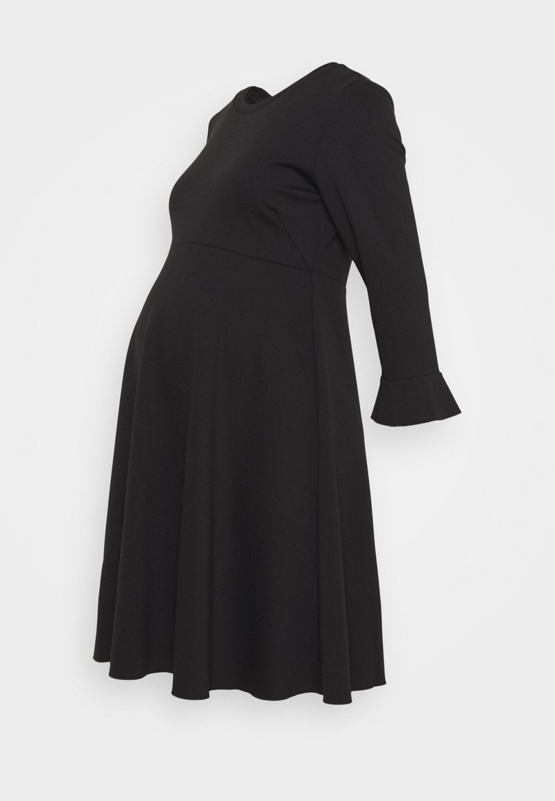 Robe de maternité noire à manches longues, jupe évasée avec un léger détail volanté aux poignets, présentée sur un fond uni.