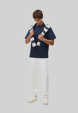 Marineblå bomulds-t-shirt med korte ærmer, parret med hvide bukser. En stribede strikket sweater lagt over skuldrene. Hvide sneakers.