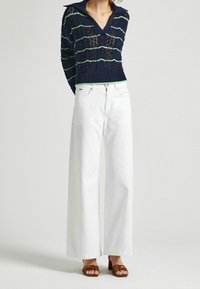 Navy knit sweater with green stripes, V-neck, and ribbed hem, paired with high-waisted white wide-leg jeans and brown strappy sandals.