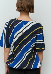 Haut rayé bleu et blanc à manches courtes, avec un col rond et une fermeture à boutons au dos. Tissu léger et texturé.