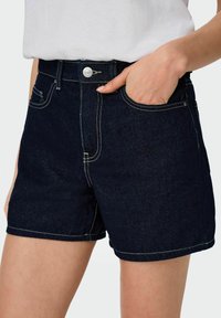 Tumši zilo džinsu šorti ar kontrastējošām baltām šuvēm, ar priekšējo kabatu, jostu cilpiņām un sudraba aksesuāriem jostas vietā.