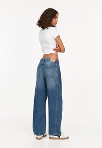 Jeans din denim albastru cu talie înaltă și picior larg, cu un ton deschis, având două buzunare în spate și o etichetă din piele bej pe talie.