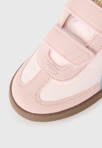 Rosa sneakers med en kombination av mjuk mocka och strukturerad tyg, med kardborreband och en brun gummisula. Accenterade med ljusblå detaljer.