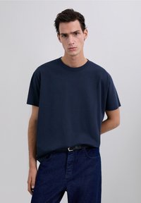 Marineblauw katoenen T-shirt met korte mouwen, een ronde halslijn en een losse pasvorm, gecombineerd met donkerblauwe spijkerbroek en een zwarte riem.