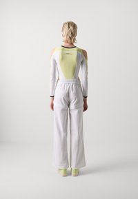 Witte brede broek met een elastische tailleband, gecombineerd met een lang mouwtop met open rug en een lichtgroene inzet en uitgesneden mouwen.