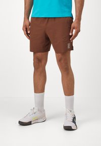 Brown shorts with a minimalist design, featuring a side pocket and a small logo. Worn with white crew socks and multi-colored sneakers.