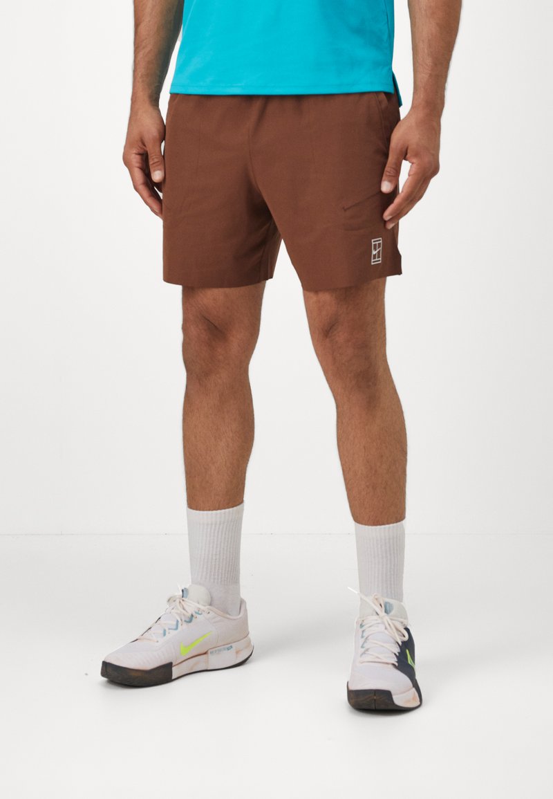 Brown shorts with a minimalist design, featuring a side pocket and a small logo. Worn with white crew socks and multi-colored sneakers.