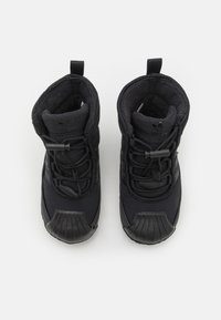 Ett par svarta Adidas vinterkängor med vadderad inredning, snörning fram och dragflikar på en vit bakgrund.