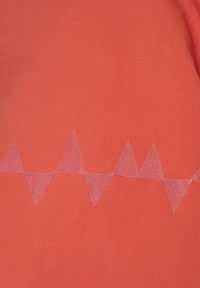 Koralstof med en tekstureret overflade har et horisontalt mønster af transparente trekantede former hen over midten.