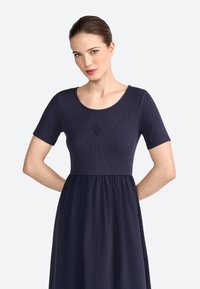 Robe bleu marine avec un haut côtelé et des manches courtes, présentant une jupe froncée et un subtil détail de logo sur la poitrine. Texture lisse dans l'ensemble.