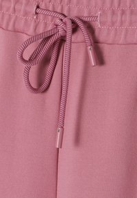 Light pink sweatpants with a textured fabric. Features a matching drawstring and metallic aglets, emphasizing a simple, sporty design.