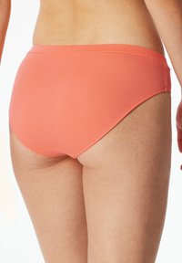 Koraalrode bikini onderkant met een naadloze tailleband en een gematigde snit. De stof lijkt glad met minimale stikseldetails.