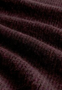 Ciemnofioletowa tkanina o teksturowanym, prążkowanym wzorze i miękkiej, puszystej powierzchni, z delikatnymi faldami i falami w materiale.