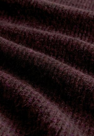 Dunkellila Stoff mit einer strukturierten, gerippten Musterung und einer weichen, flauschigen Oberfläche, die sanfte Falten und Wellen im Material zeigt.