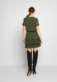 Vestido floral verde con volantes en capas, mangas cortas, cintura elástica, combinado con botas de gamuza negras hasta el muslo y tacones puntiagudos.