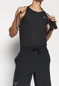 Černý tank top s odvodem vlhkosti a texturovaným povrchem, spárovaný s volnými černými šortkami, které mají logo na levé noze a stahovací pas.