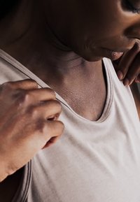 Osoba upravujúca výstrih svetlej bezrukávovej blúzky, so zameraním na hruď a ruky.