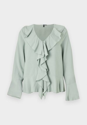 Blusa verde chiaro con scollatura a V, dettaglio drappeggiato sul davanti, maniche lunghe con polsini a campana e una silhouette fluida.