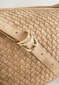 Geweven beige suède handtas met een gladde textuur en gouden dubbele ringhardware. Voorzien van een klepsluiting en accentstiksels.
