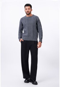 Pull en tricot gris avec un motif en câble, associé à un pantalon large noir et des chaussures noires épaisses. Design minimaliste, texture légère.