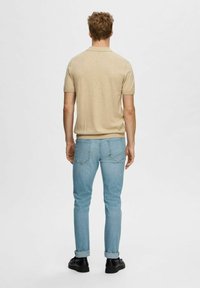 Beige polo-shirt met korte mouwen, gecombineerd met lichtblauwe slim-fit jeans, met een achterzak ontwerpen en zwarte schoenen.
