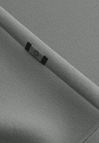 Grau Stoff mit einer strukturierten Oberfläche, versehen mit einem schwarz-weißen Etikett mit einem Kreuzsymbol. Das Material wirkt weich und ordentlich gefaltet.