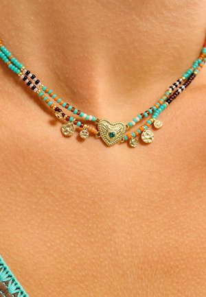 Collier multirang avec des perles turquoise, orange et noires. Comprend un pendentif cœur en or avec une pierre bleue, accompagné de petits charms en or.