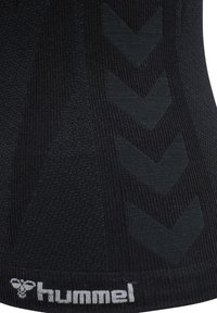 Gros plan sur un tissu noir avec un motif chevron texturé et le logo blanc « hummel » sur le bord inférieur.