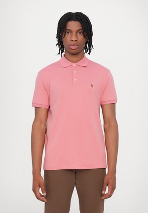 Tricou polo roz deschis cu guler clasic, trei butoane și un mic logo brodat pe partea stângă a pieptului. Manșete scurte rulate.